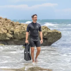 גבר בחליפת שורטי יוצא מהים אל הסלעים כשבידיו סנפירים ומסכה